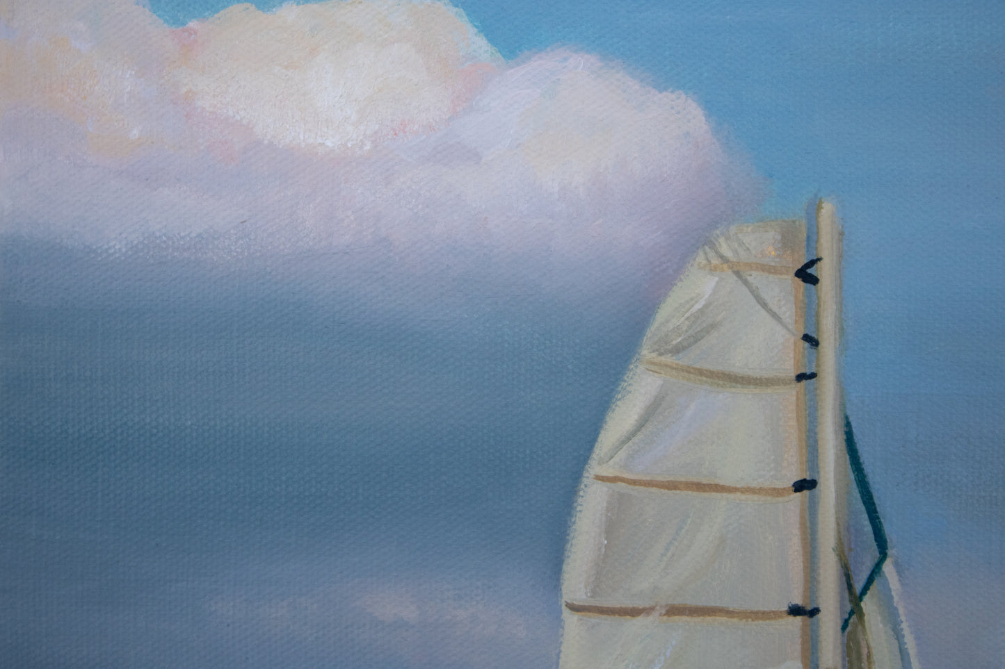 Close up of a sailboat with a white sail against a blue sky with clouds