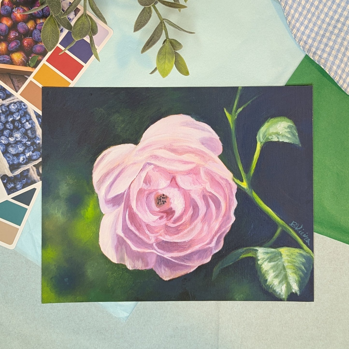 Painting print of a pink rose on a dark background with color swatches and fabric in the background.