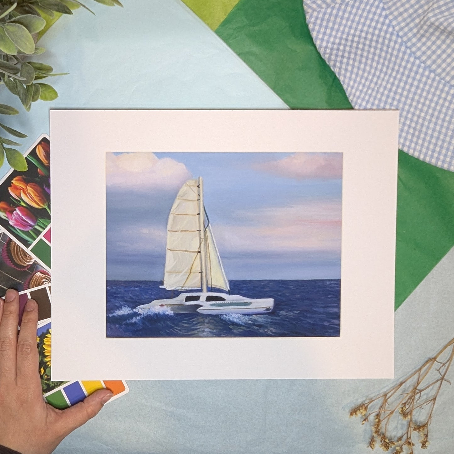 Framed artwork of a sailboat on a blue sea with a hand holding the frame.