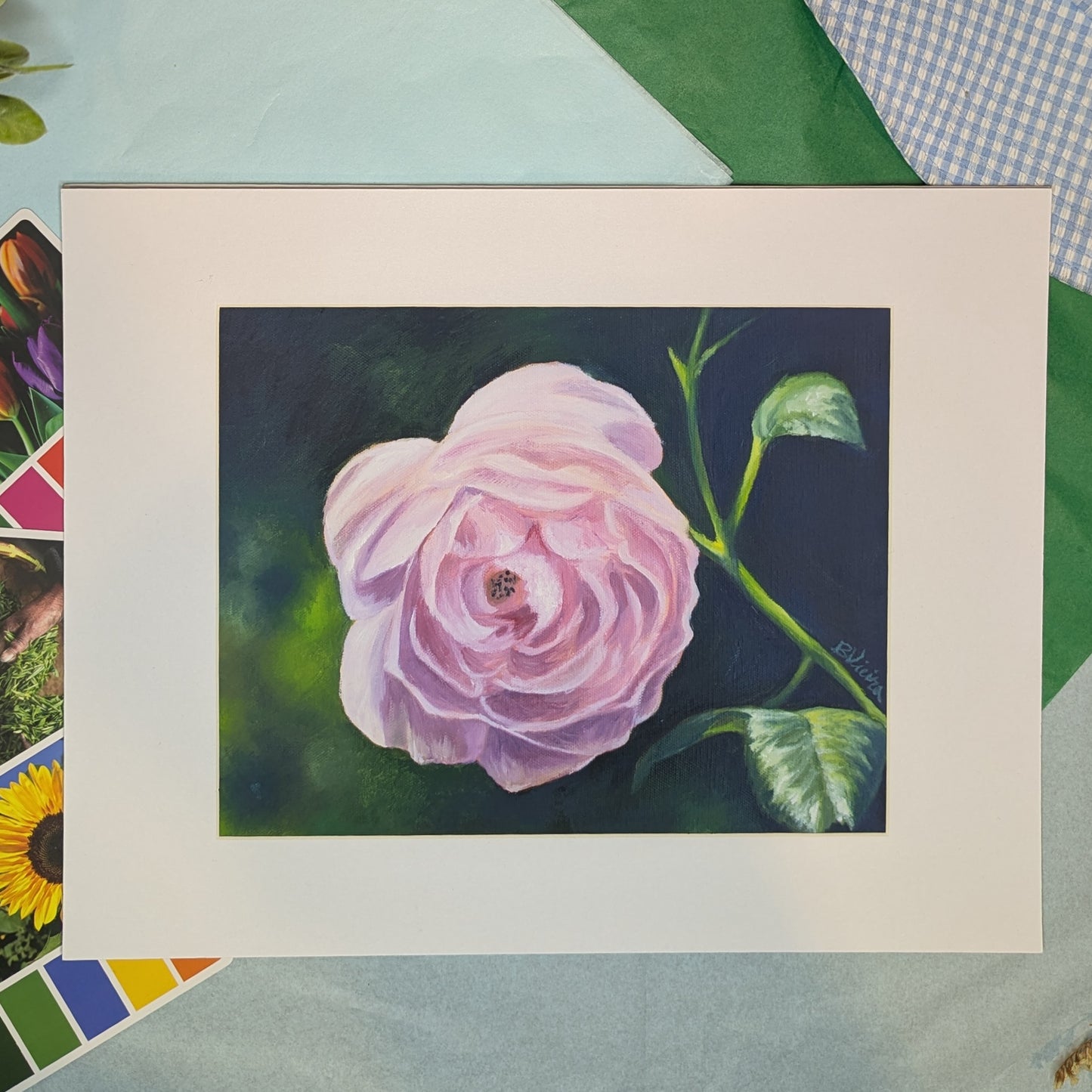 matted print of a painting of a pink rose on a colorful background