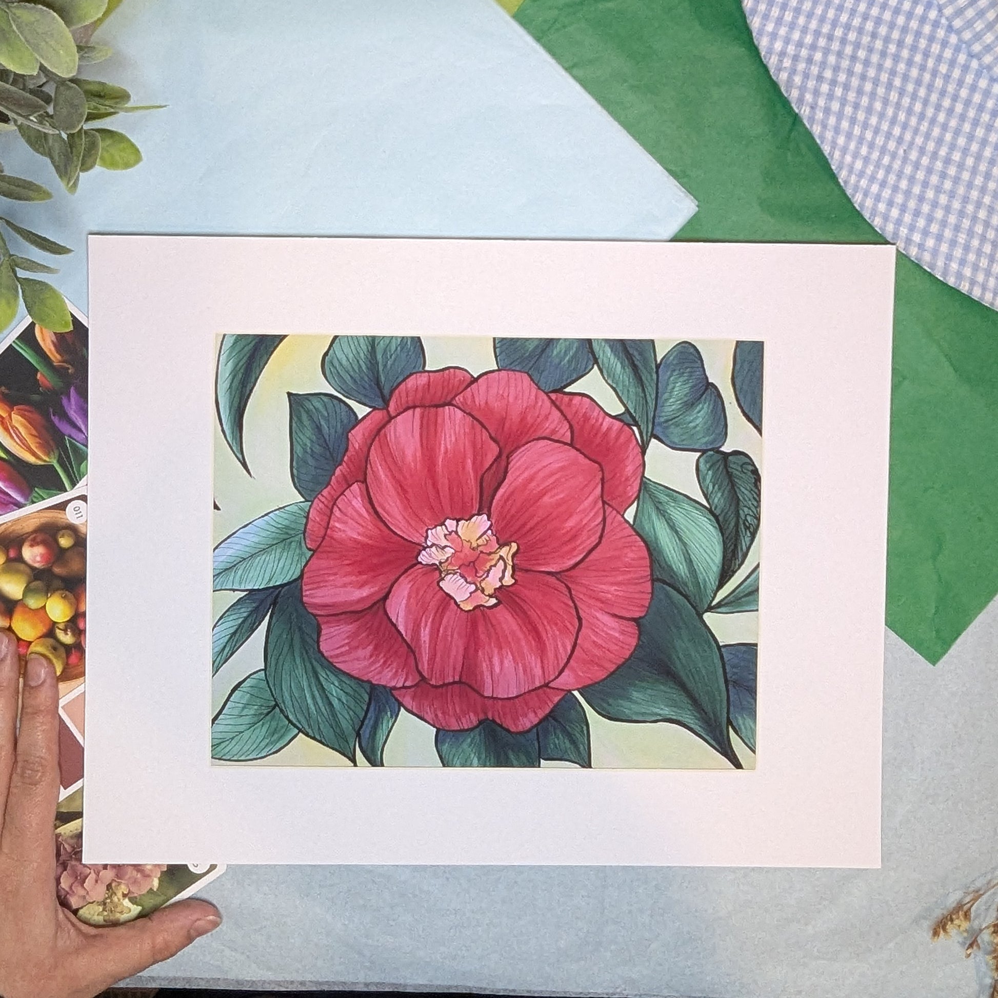 matted artwork of a pink flower with green leaves on a colorful background