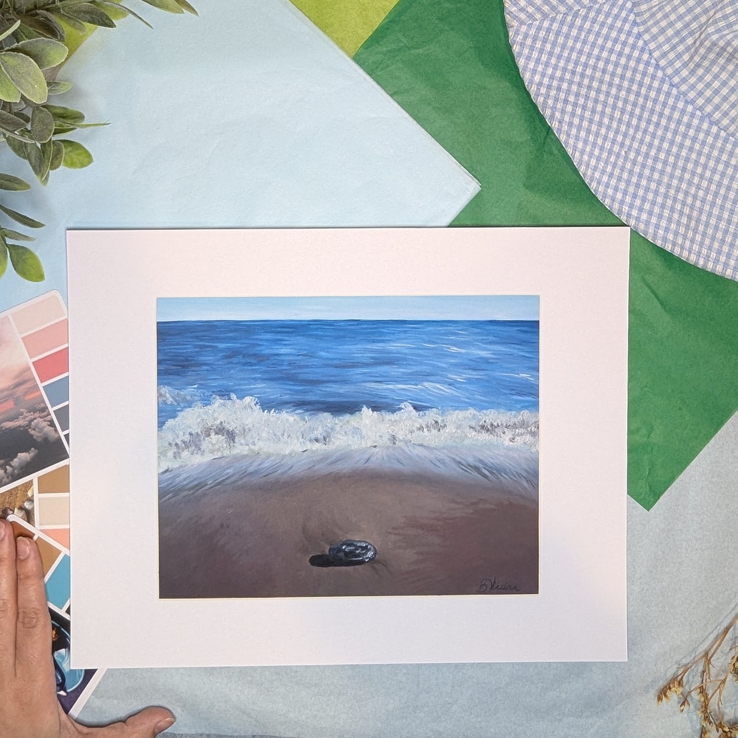 artwork of a beach scene with waves and sand, next to a hand on a colorful background.