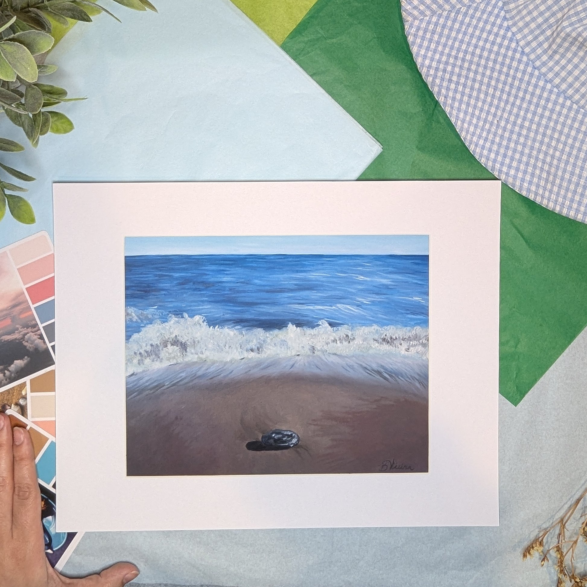 artwork of a beach scene with waves and sand, next to a hand on a colorful background.
