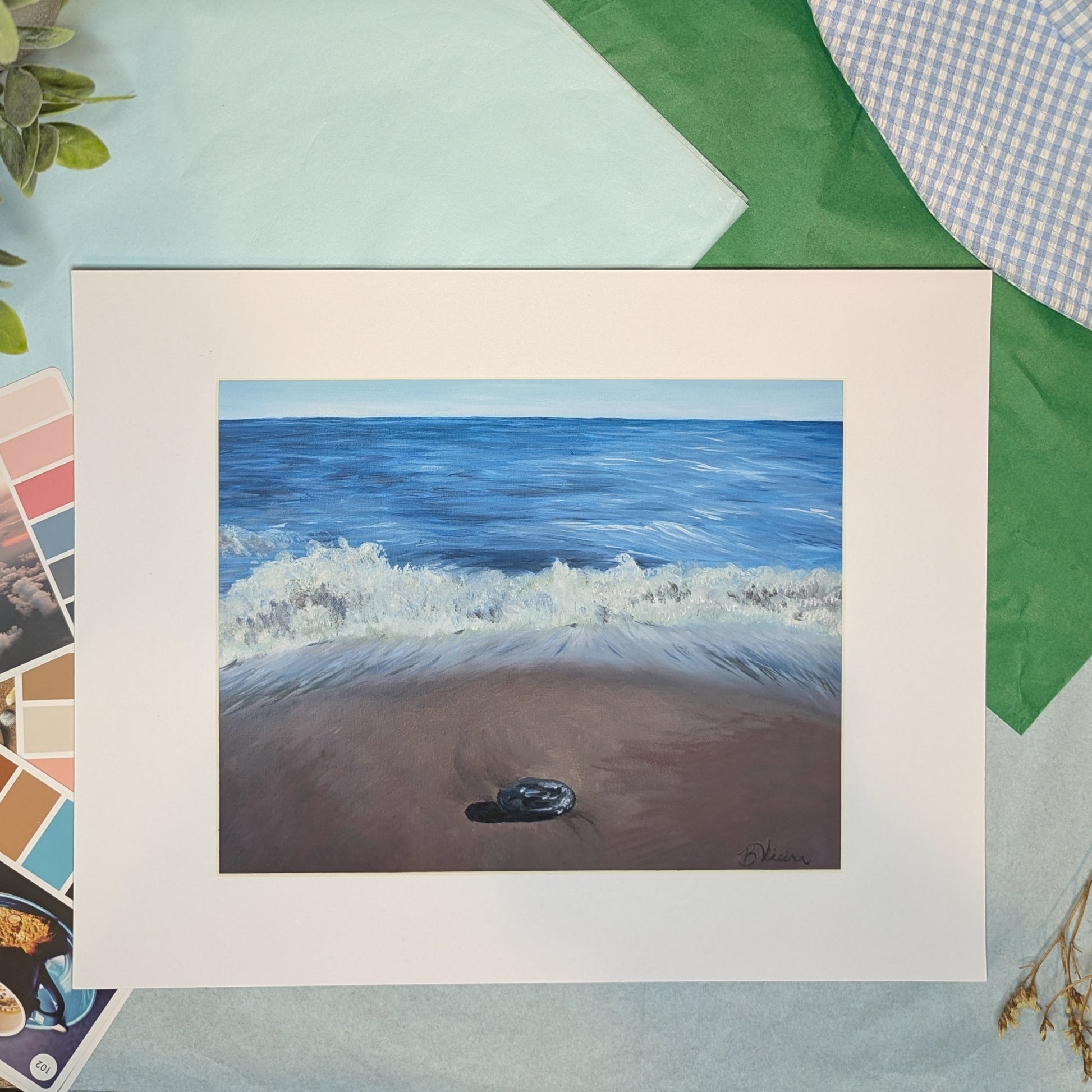 Artwork of a beach scene with waves and a pebble, surrounded by color swatches and fabric samples.