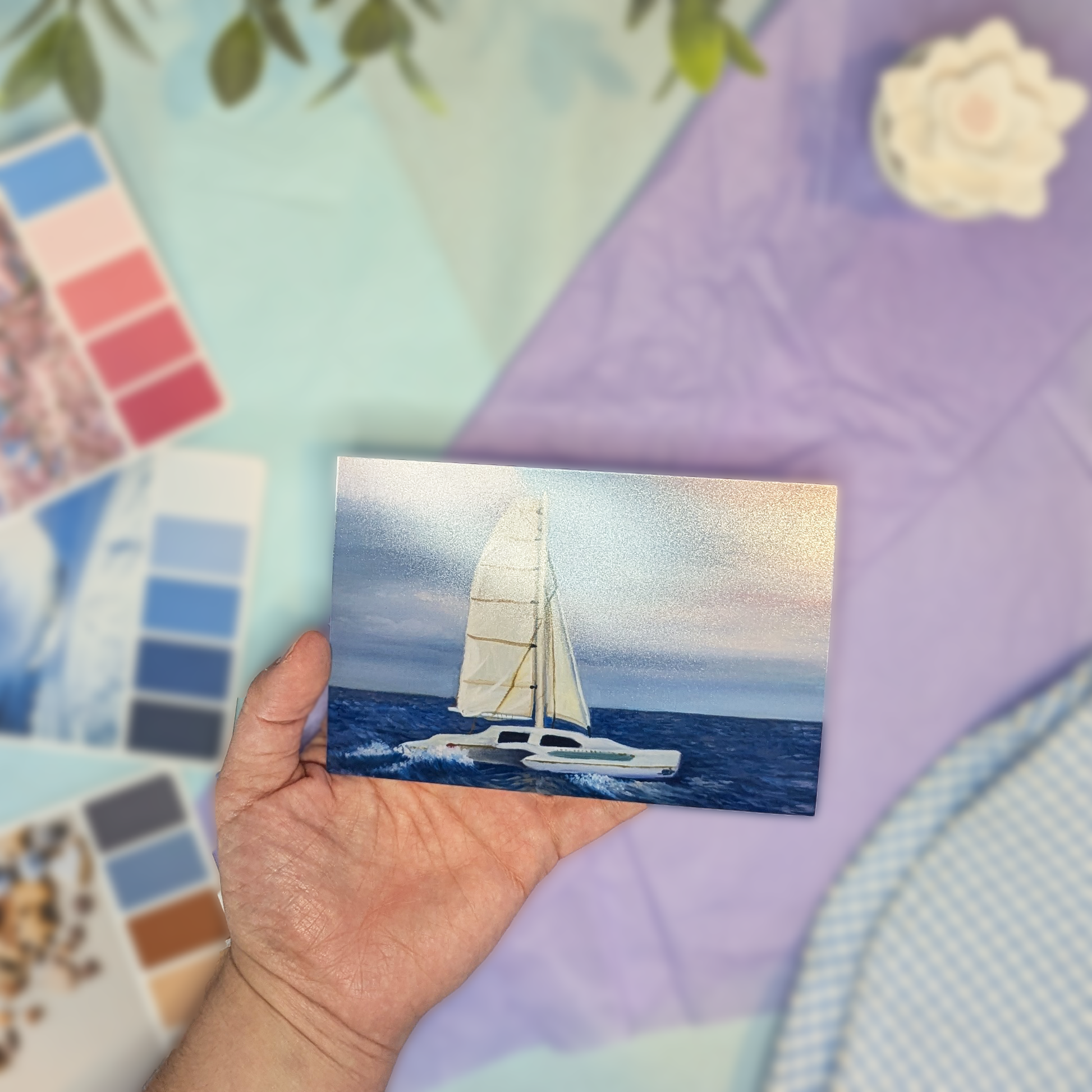 Hand holding a print with a sailboat on a colorful fabric background