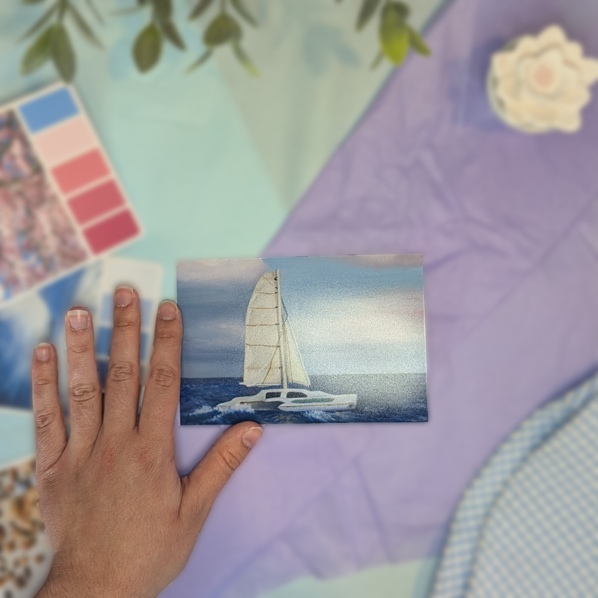 Hand holding a print with a sailboat on a colorful blurred background