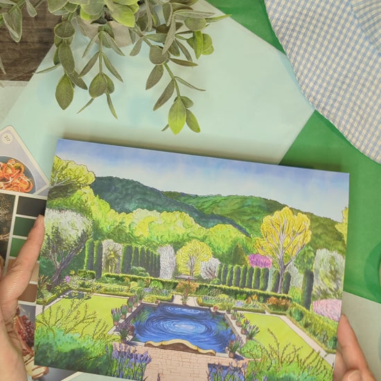 video of artist holding print of colorful illustration of trees, reflection pool and flowers