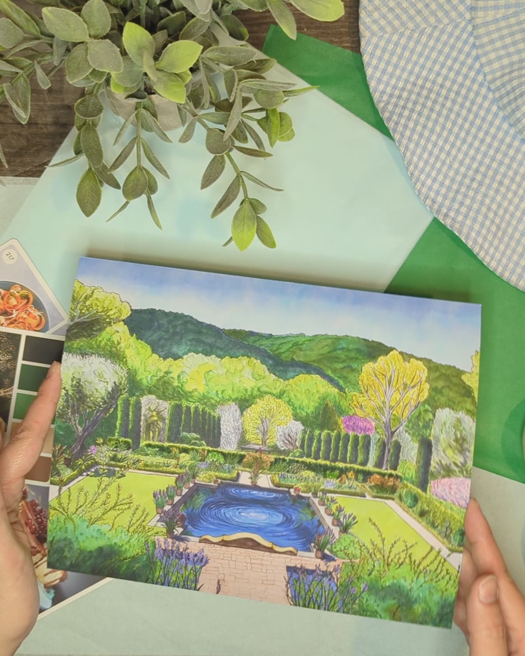 video of artist holding print of colorful illustration of trees, reflection pool and flowers