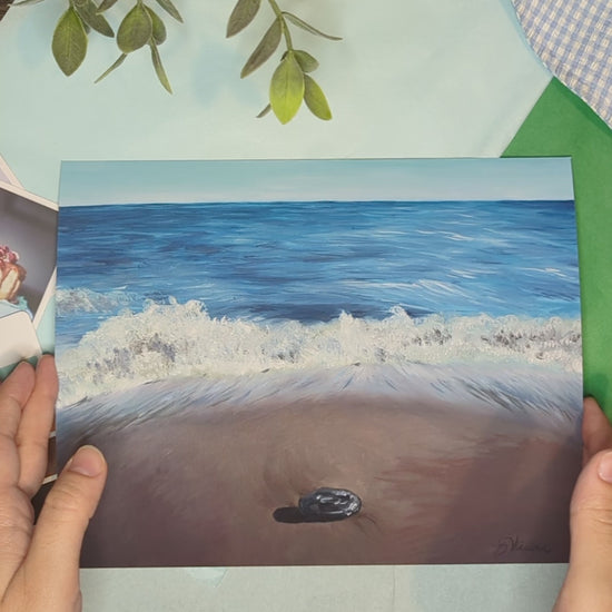 video of the artist's hands holding an oceanscape print of waves crashing at the shore