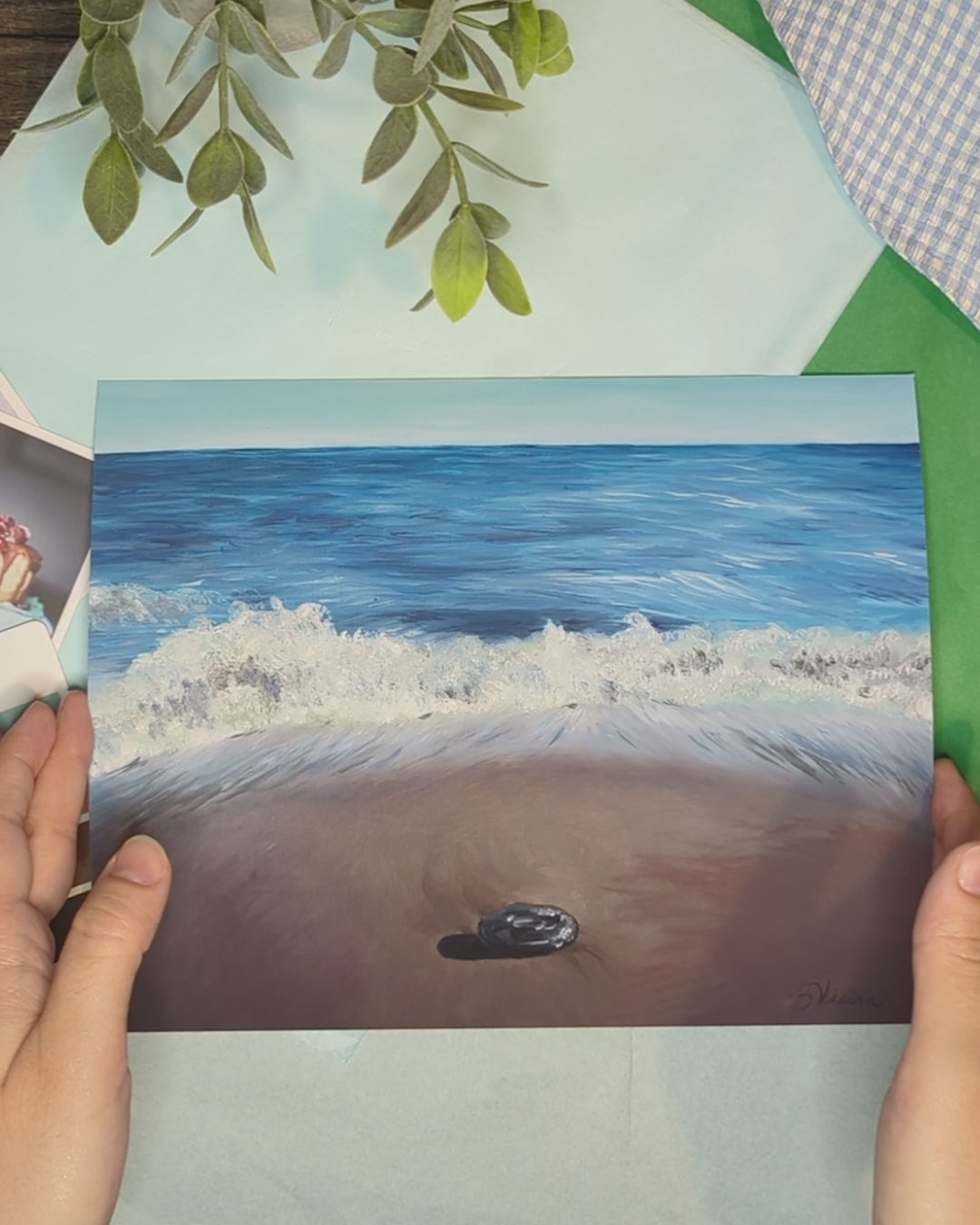 video of the artist's hands holding an oceanscape print of waves crashing at the shore